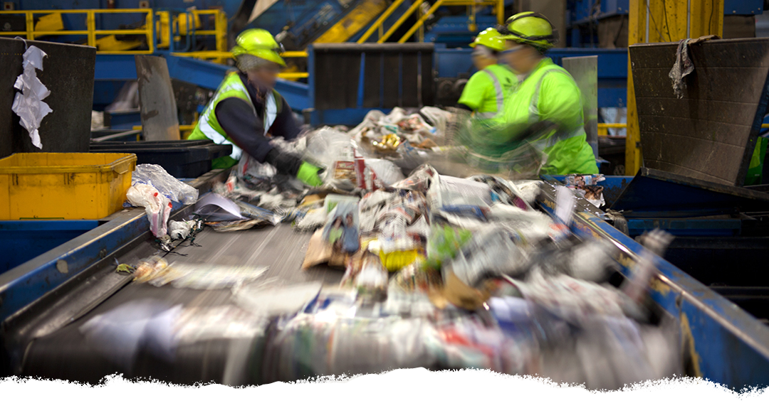 Workers at a materials processing facility sort recyclers on a fast-moving conveyor belt.